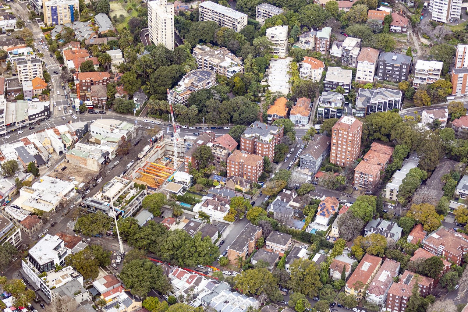 An aerial view of buildings, tree-lined streets and construction cranes